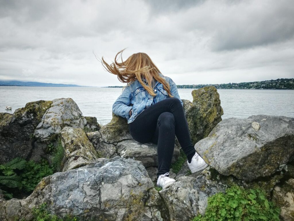 Woman With Blue Denim Collared Button-up Jacket and Black Jeans Sitting on Gray Rock Watching Lakeview