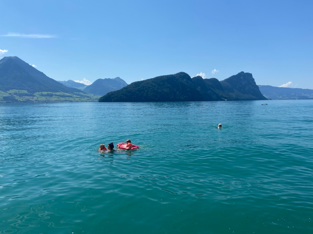 People enjoying a sunny summer day swimming in the turquoise waters of Lake Lucerne, reminding travelers what to pack for Switzerland, including swimsuits and summer gear.