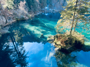 Turquoise blue Blausee in the Bernese Oberland, Switzerland, surrounded by vibrant autumn foliage reflecting on the crystal-clear water during fall.