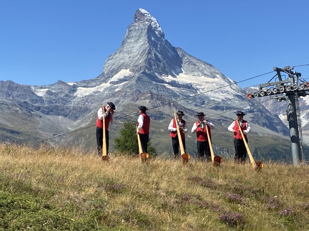 Alphorn players performing for Swiss National Day with the iconic Matterhorn in the background, one of the customs and traditions in Switzerland that beautifully blends music, culture, and stunning natural landscapes.