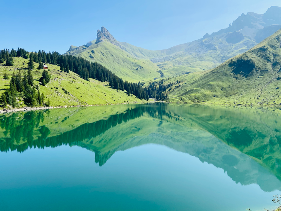 Lake Bannalp (Bannalpsee), a beautiful mountain lake in Central Switzerland on a sunny day, with crystal-clear water reflecting the surrounding majestic mountains, framed by lush green alpine meadows.