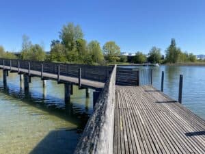 Wooden bridge leading from Hurden to Rapperswil – A long wooden footbridge stretching over the calm waters of Lake Zurich, connecting Hurden to Rapperswil, with clear blue skies.