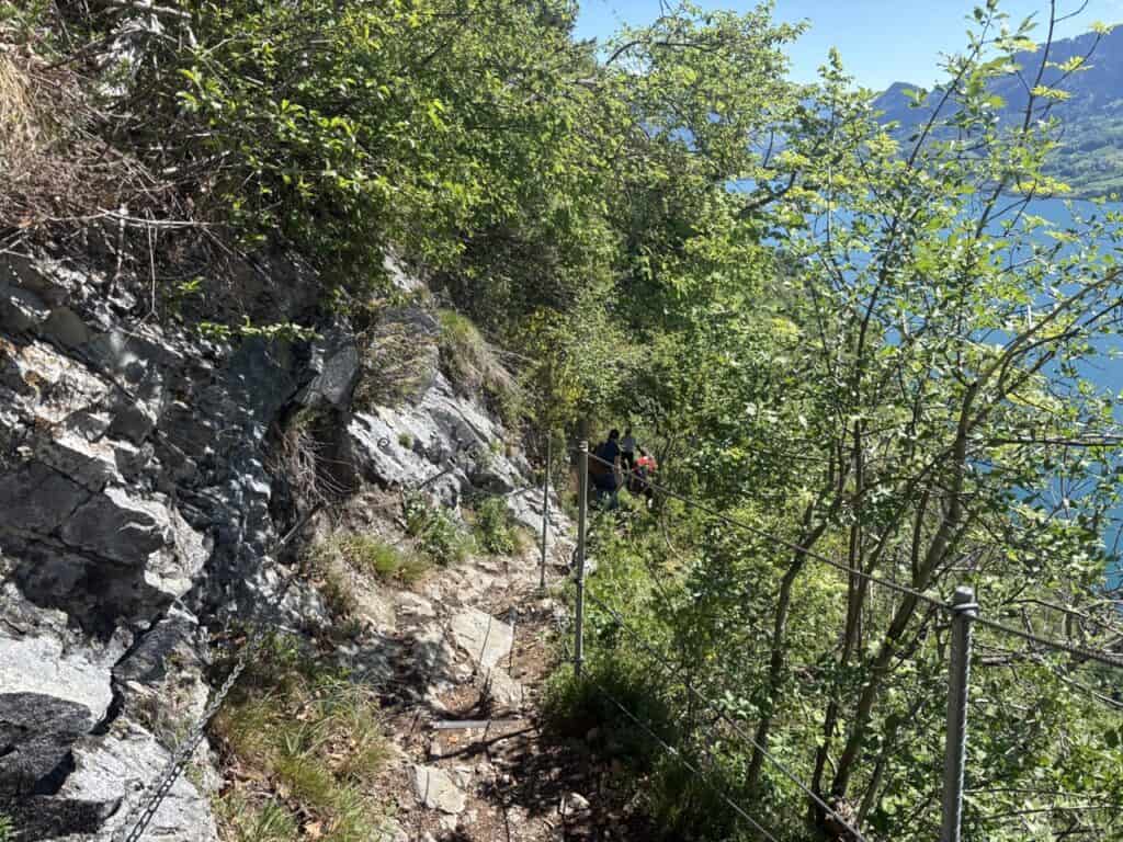 Steep rocky hiking trail secured by ropes, descending toward Quinten above Lake Walensee