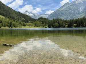 Golzernsee, a clear Swiss alpine lake in the canton of Uri, Switzerland, surrounded by rugged mountains and forested slopes under a bright sky.