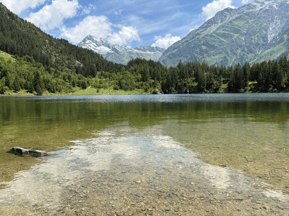 Golzernsee, a clear Swiss alpine lake in the canton of Uri, Switzerland, surrounded by rugged mountains and forested slopes under a bright sky.