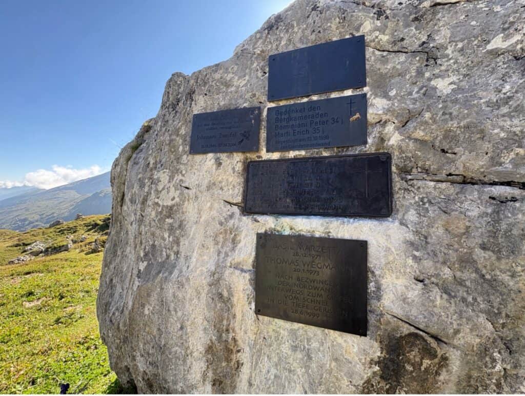 Memorial stone at Klausenpass honoring people who lost their lives at Clariden, set against alpine scenery.