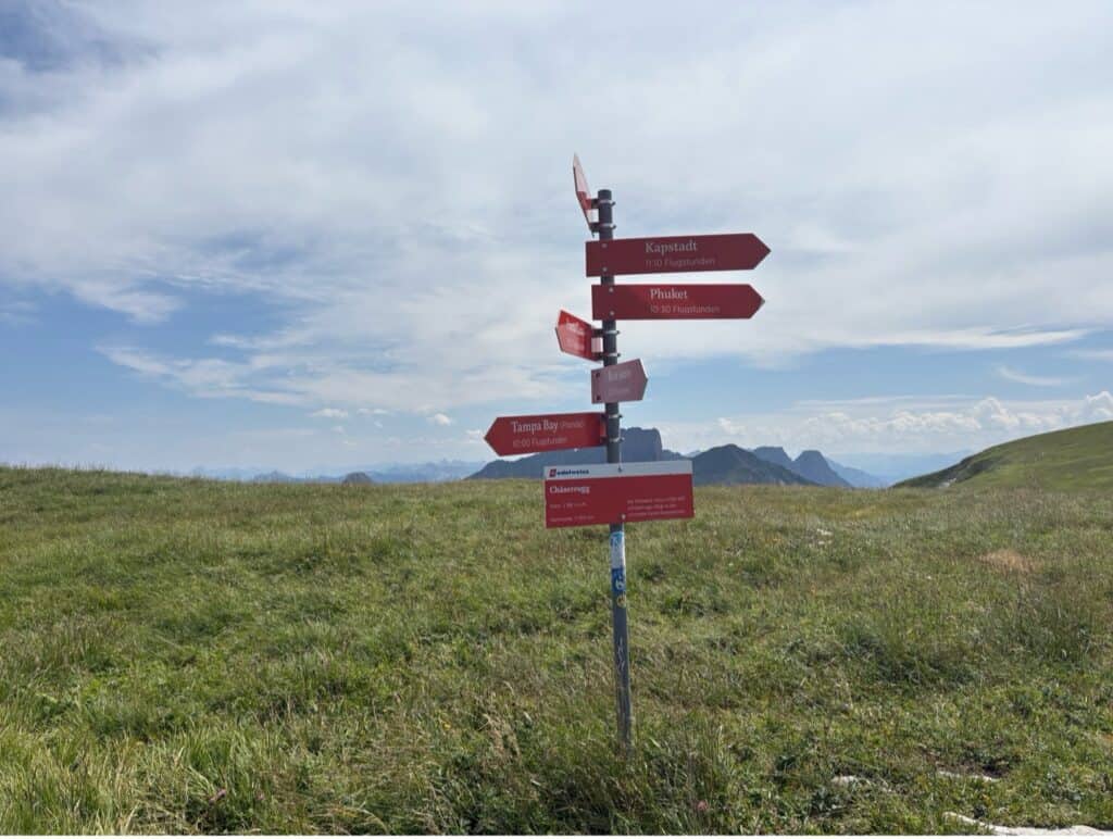 Red signpost next to Edelweiss seats on Chäserrugg showing distances to destinations around the world.