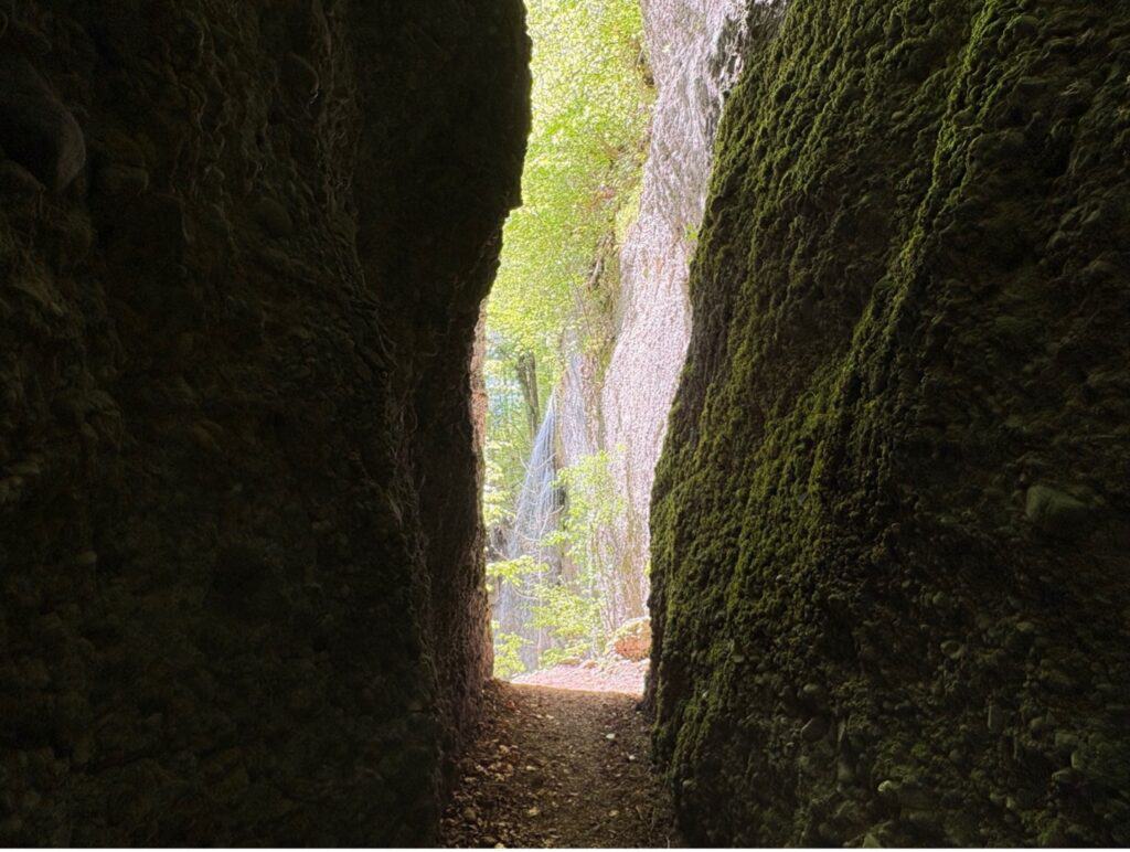 Narrow rocky opening revealing a hidden waterfall in the Äulischlucht .
