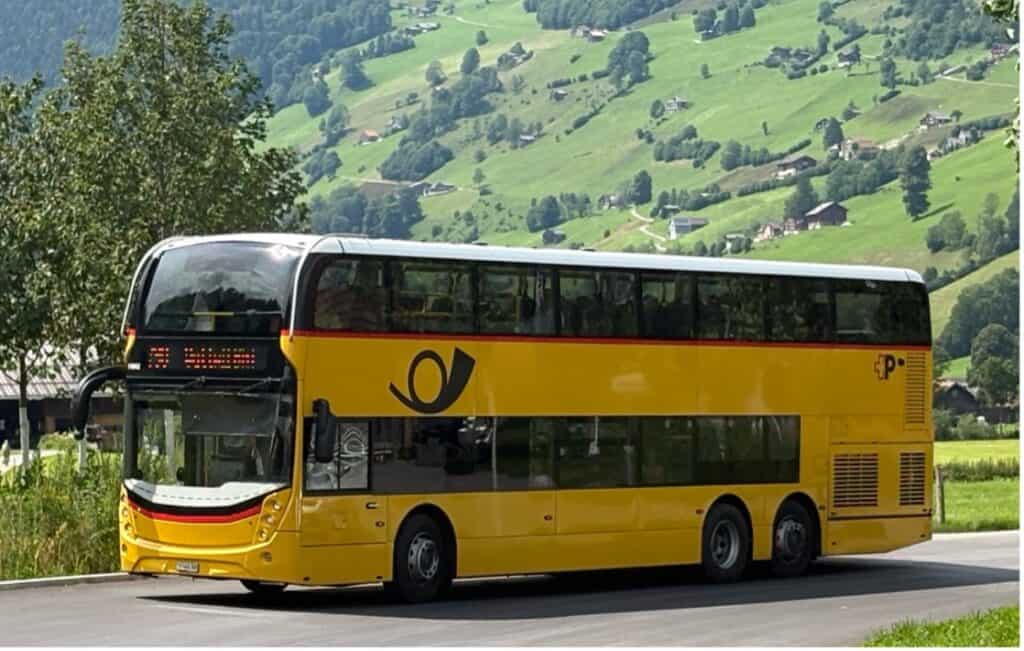 Yellow double-decker PostBus driving through the Toggenburg region in Switzerland.