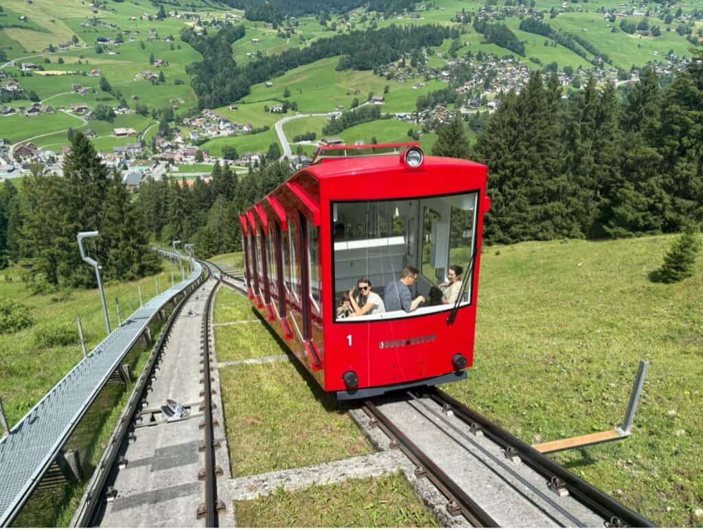 Red funicular railway traveling uphill between Chäserrugg valley station and Iltios middle station.