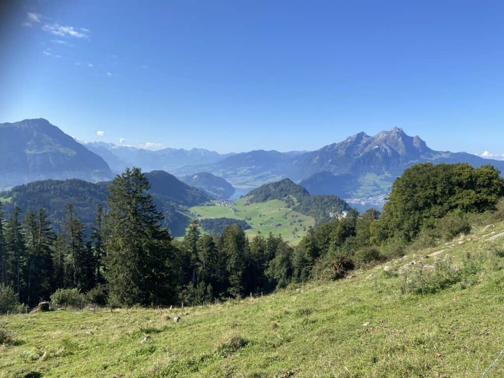 View from the Top of the Hammetschwand station overlooking green rolling hills with the blue water of Lake Lucerne and mountains shimmering in the background.