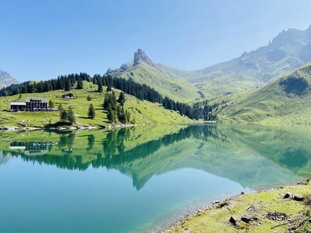 Bannalpsee in Central Switzerland, a calm alpine reservoir surrounded by green meadows and steep mountain slopes.