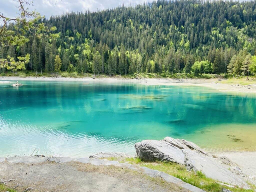 Turquoise-blue Caumasee near Flims in Graubünden, a stunning mountain lake with Caribbean-like colors surrounded by forested hills.