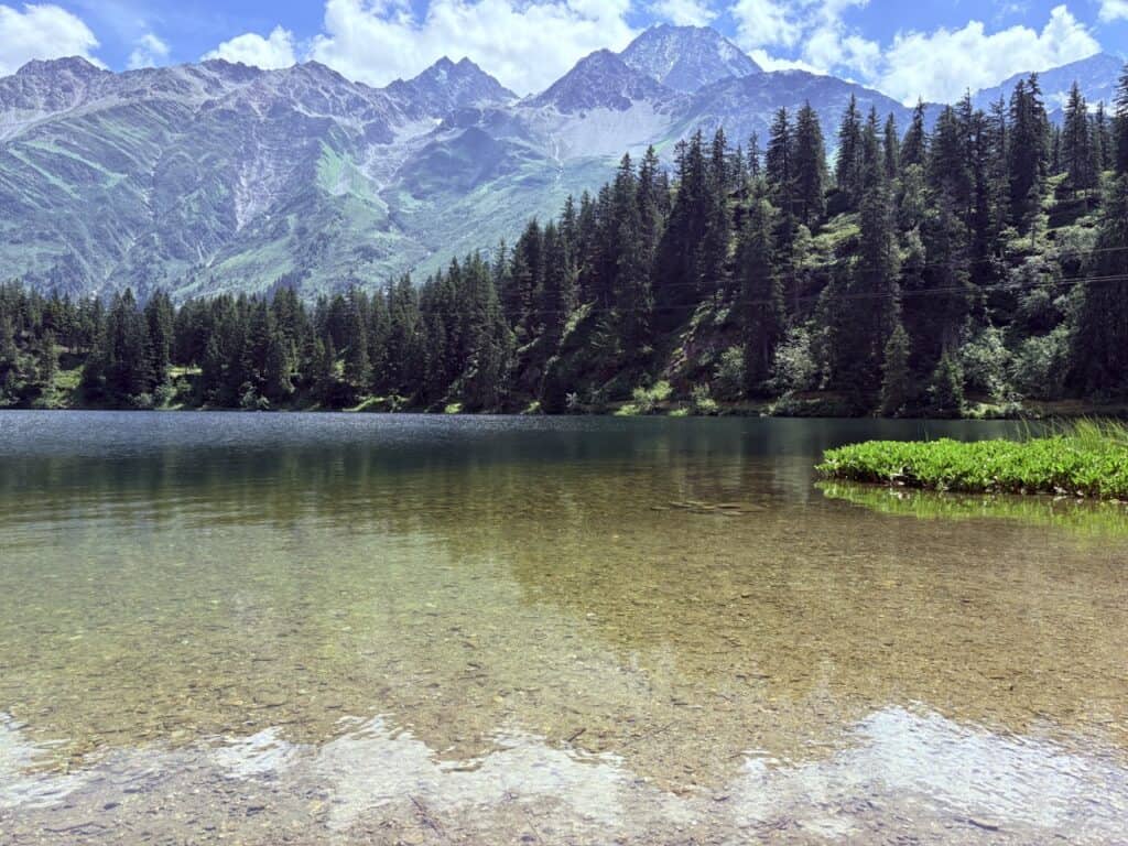Golzernsee in the canton of Uri on a clear day, a tranquil mountain lake surrounded by forest and rugged mountain scenery.