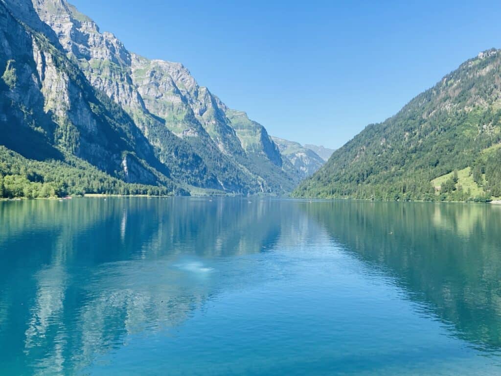 Klöntalersee, a crystal-clear fjord-like lake in the canton of Glarus, surrounded by steep rock walls and alpine peaks.