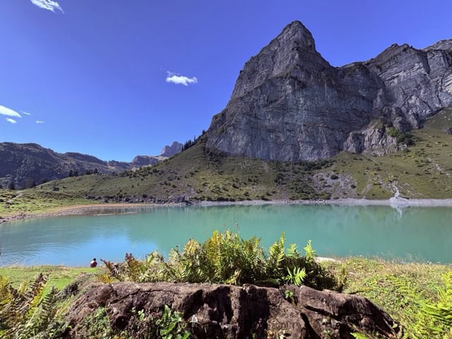 Oberblegisee in the canton of Glarus on a clear day, a Swiss alpine lake with deep blue water nestled beneath dramatic mountain cliffs.