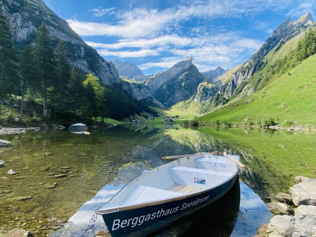 Seealpsee in the Alpstein region of Appenzell, a clear alpine lake with rowing boat and lush meadows beneath dramatic mountains.