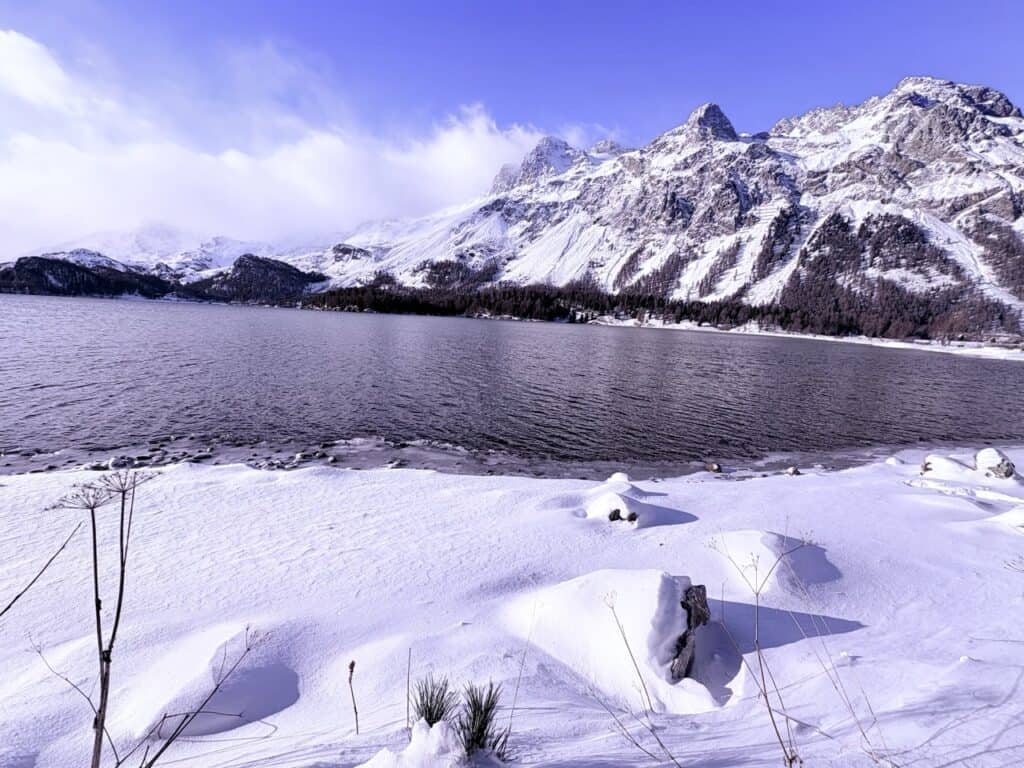 Snow-covered landscape and peaks surrounding Silsersee in the Engadine Valley of Switzerland in December, the lake still unfrozen and reflec.