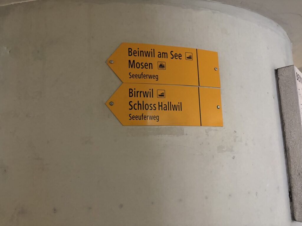 Yellow hiking signpost pointing toward Lake Hallwil and Hallwyl Castle