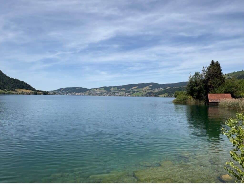 Panoramic view of Lake Ägeri surrounded by rolling green hills and scenic Swiss countryside.
