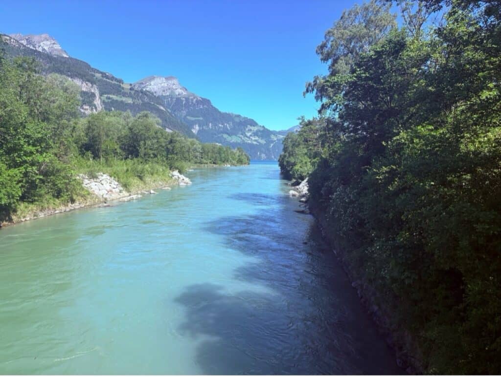 Scenic view from a bridge looking down at the flowing Reuss river surrounded by green riverbanks.