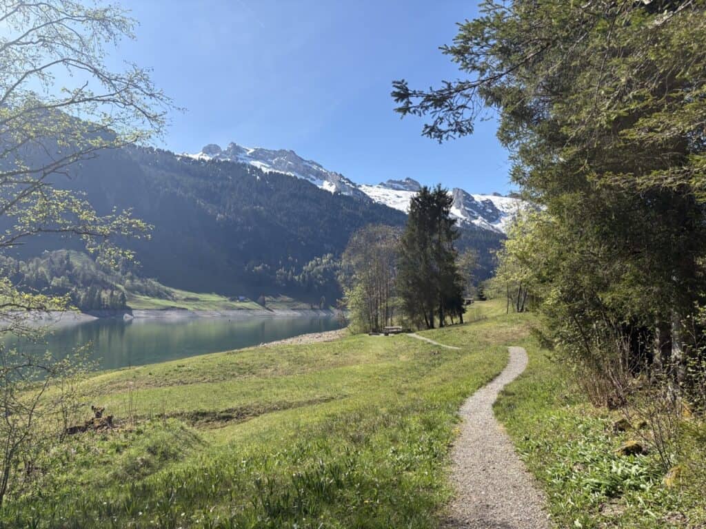 Walking path following the shore of Wägitalersee with snow capped peaks in the background