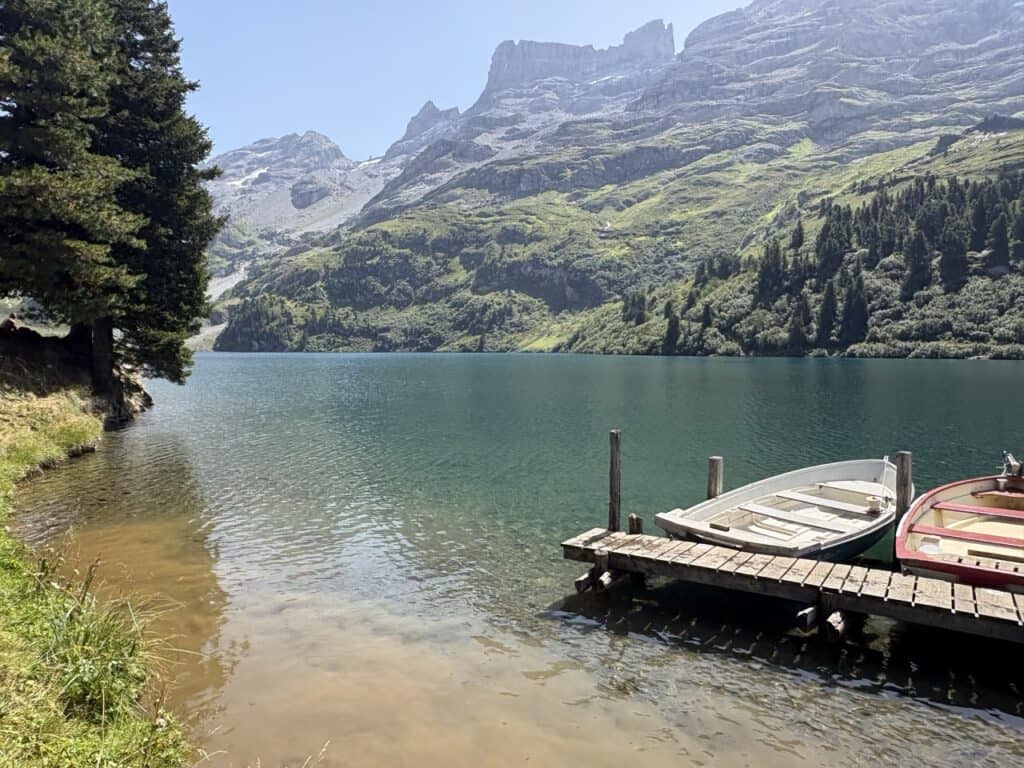 Beautiful view of turquoise-blue Engstlensee with a boat resting on the shore, surrounded by stunning mountain scenery along the Four Lakes Hike in Switzerland.